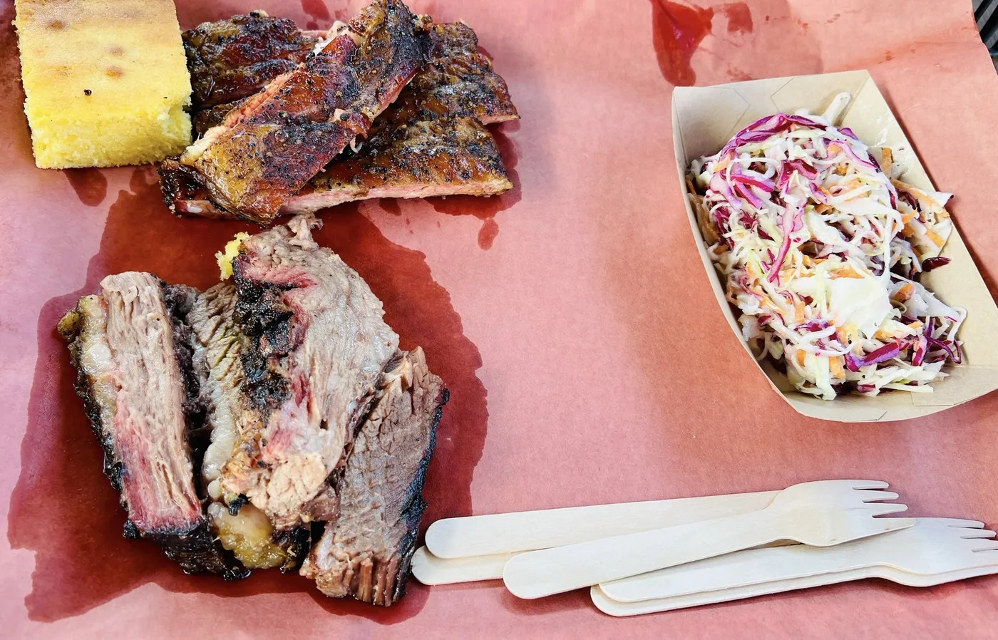 Sliced brisket and pork ribs on pink butcher paper with coleslaw